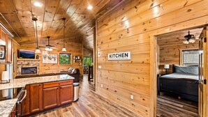Interior de una cabaña de madera con cocina, comedor y habitación.