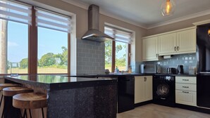 A modern kitchen with a large island, bar stools, a dishwasher, a washing machine, and a view of the outdoors. - Tranquil Carney Commons Cottage - Sleeps 10 (Congor)