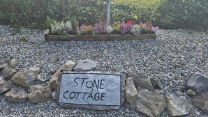 A sign reading "STONE COTTAGE" on a gravel path with a flower bed in the background. - Tranquil Carney Commons Cottage - Sleeps 10 (Congor)