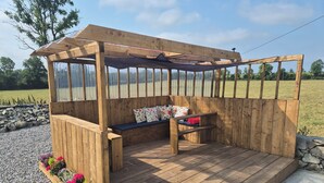 A wooden outdoor seating area with a bench and a table, surrounded by a wooden fence and a gravel path. - Tranquil Carney Commons Cottage - Sleeps 10 (Congor)