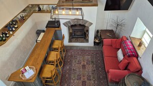 A cozy living area with a fireplace, a red sofa, a wooden dining table with chairs, a kitchen area with a wine rack, and a TV mounted on the wall. - Tranquil Carney Commons Cottage - Sleeps 10 (Congor)