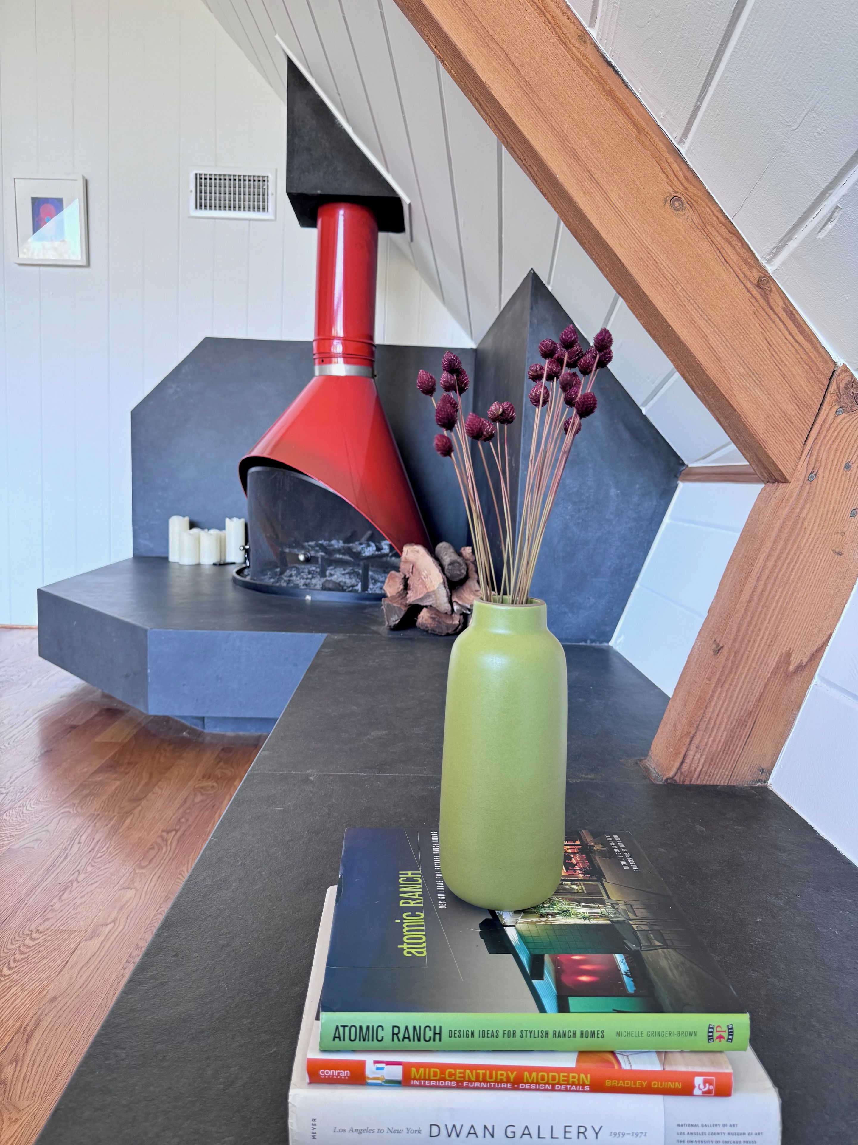 Ein modernes Interieur mit Kamin, einer grünen Vase mit Trockenblumen und einem Bücherstapel auf einem Tisch.
