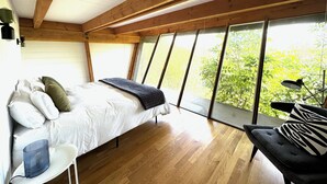 A bedroom with a bed, a chair, and a large window with a view of trees. - Architectural Marvel in Hollywood Hills with Views (Los Angeles)