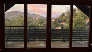 A room with a large window overlooking a mountainous landscape with a sunset. - Architectural Marvel in Hollywood Hills with Views (Los Angeles)