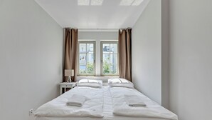 Een tweepersoonsbed met witte lakens en handdoeken, een nachtkastje met lamp en een raam met gordijnen.