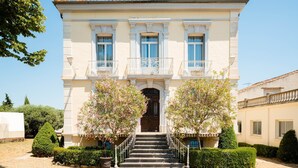 A two-story building with a symmetrical facade, a central entrance with a dark wooden door, and a balcony with white railings. - Maison de Maître 4* Piscine, Vignobles & Plages 6 pers. - Coeur Cristal (Magalas)