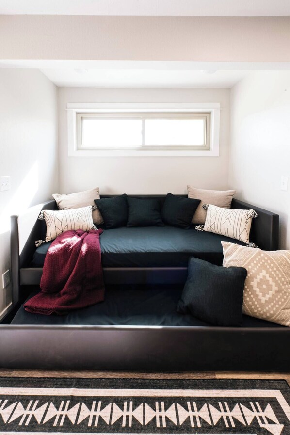 A cozy corner with a dark-colored sofa, multiple pillows, a red throw blanket, and a patterned rug.