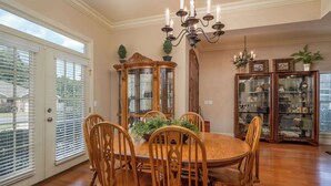 Comedor con mesa y sillas de madera, una araña y armarios con puertas de cristal que exhiben objetos decorativos.