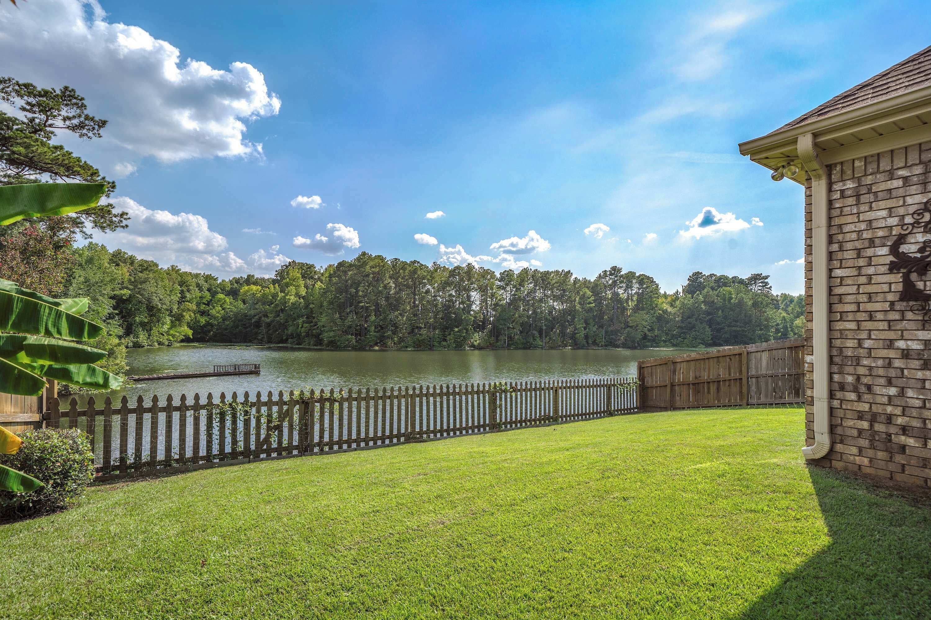 A backyard with a wooden fence, a grassy lawn, and a lake.