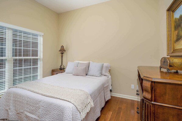 A bedroom with a bed, nightstand, lamp, dresser, and a painting on the wall.