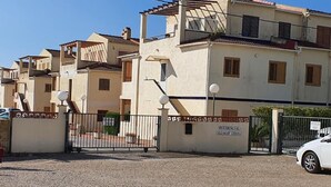 A residential area with a gated entrance, a sign indicating 'RESIDENCIAL ALCANAP COSTA', and a white car parked nearby. - Alcanar Costa (CT)