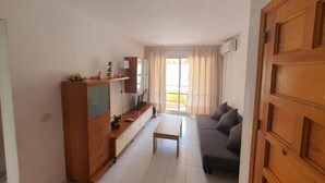 A compact living space with a sofa, a wooden cabinet, a television, and a window with curtains. - Alcanar Costa (CT)