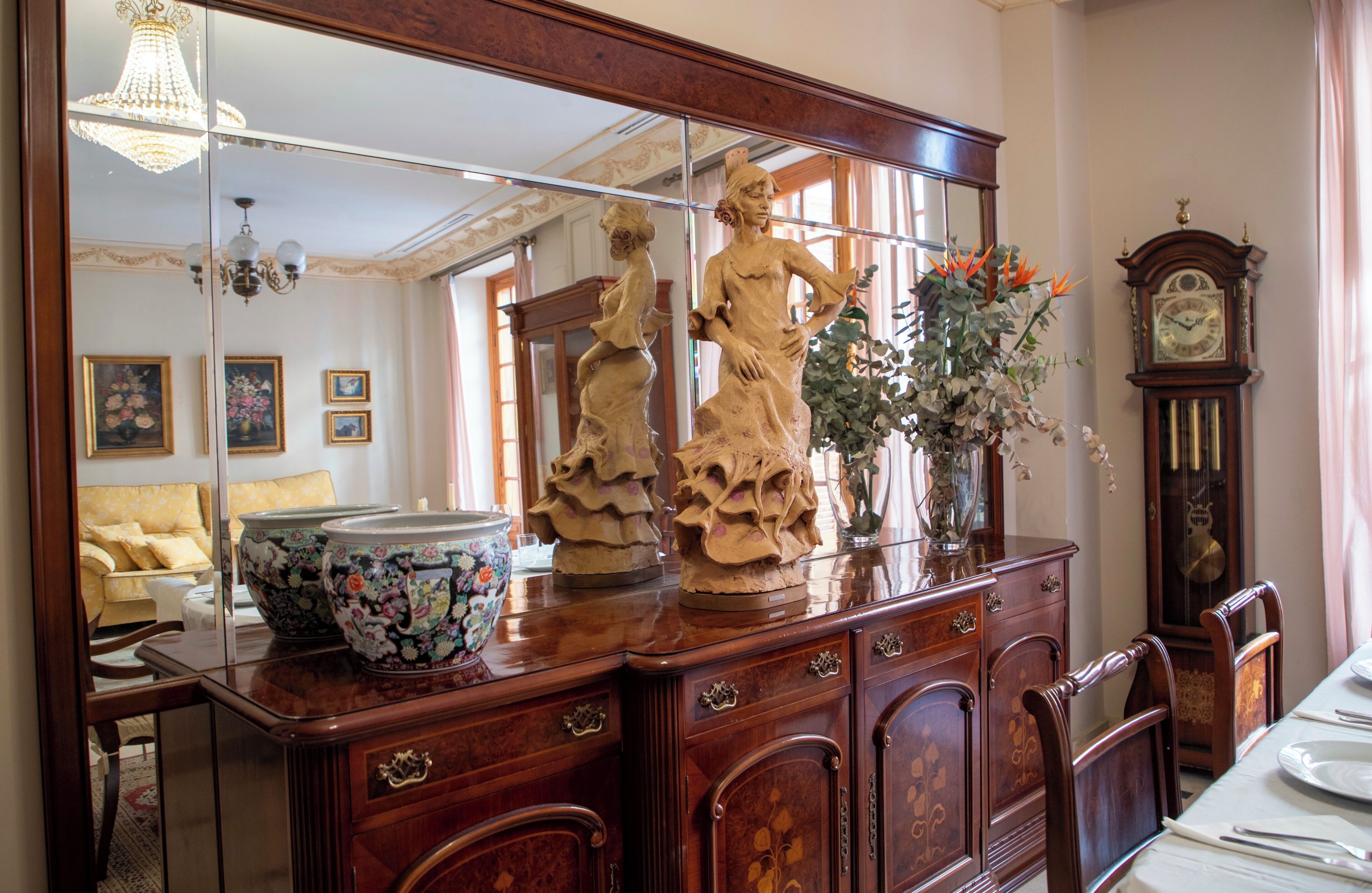 A dining area with a wooden table, chairs, a large mirror, and a clock on the wall.