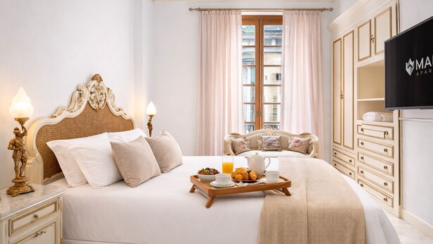 Un dormitorio elegante con una cama grande, mesitas de noche, televisión y una ventana con cortinas.