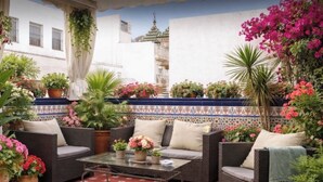 Un área de estar al aire libre con mobiliario de mimbre, una mesa con cubierta de vidrio y plantas en macetas.