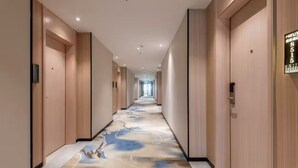 A hotel hallway with a long corridor, wooden doors, and a floor with a blue and white abstract design. - Manli Hotel (Foshan)