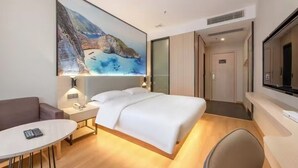 A modern hotel room with a large bed, a bedside table with a lamp, a small round table, and a TV. - Manli Hotel (Foshan)