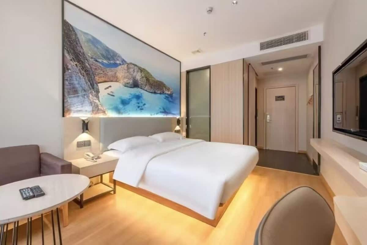A modern hotel room with a large bed, a bedside table with a lamp, a small round table, and a TV.