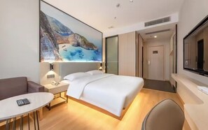 Una habitación de hotel moderna con una cama grande, una mesita de noche con lámpara, una pequeña mesa redonda y un televisor.