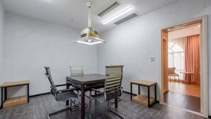 A conference room with a rectangular table, two chairs, a ceiling-mounted projector, and a door leading to another room. - Manli Hotel (Foshan)