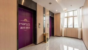A hotel corridor with purple doors, a small wooden cabinet, and a large window with curtains. - Manli Hotel (Foshan)