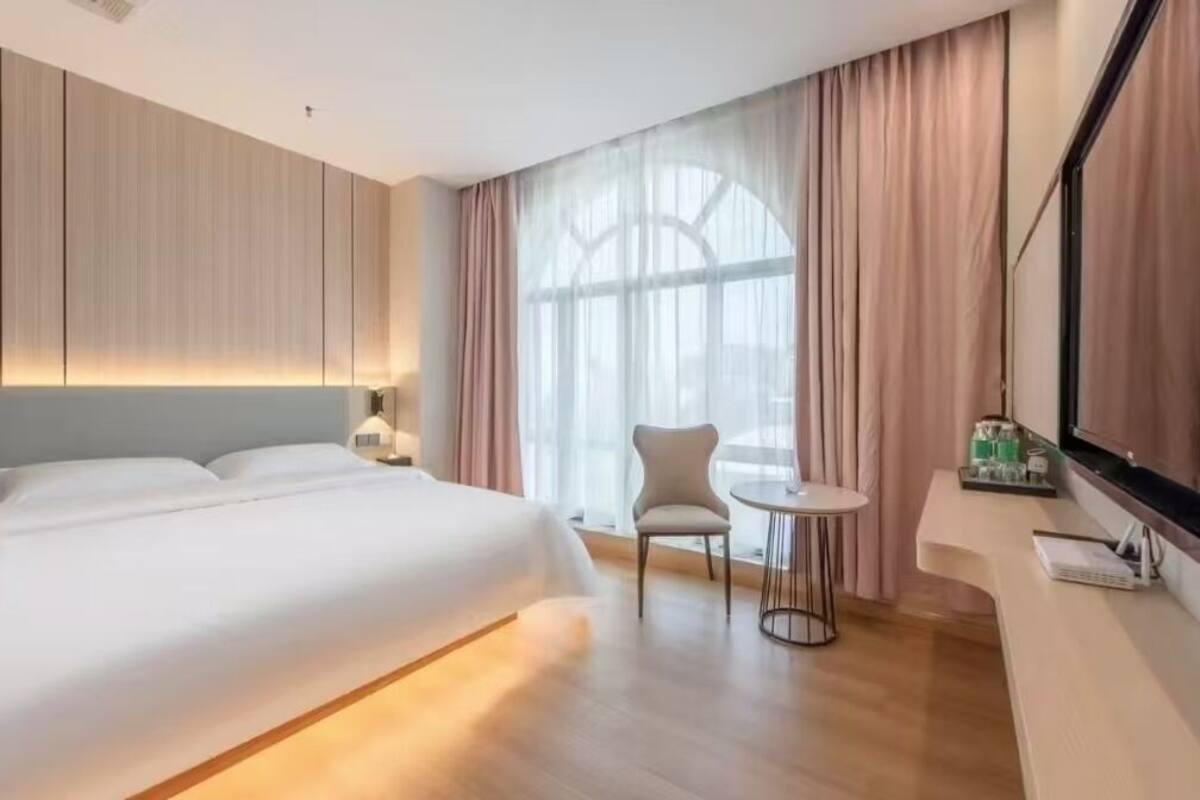 A hotel room with a large bed, a small round table, a chair, and a large window with curtains.