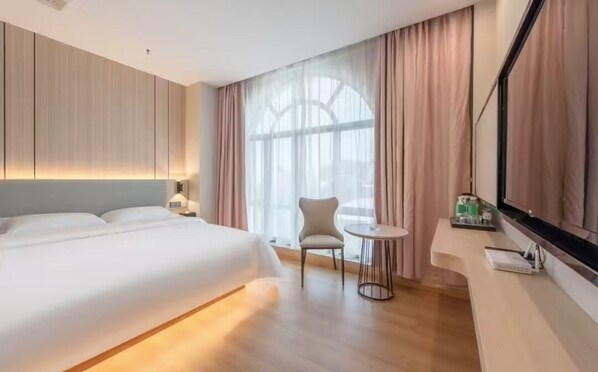 Une chambre d’hôtel avec un grand lit, une petite table ronde, une chaise et une grande fenêtre avec des rideaux.