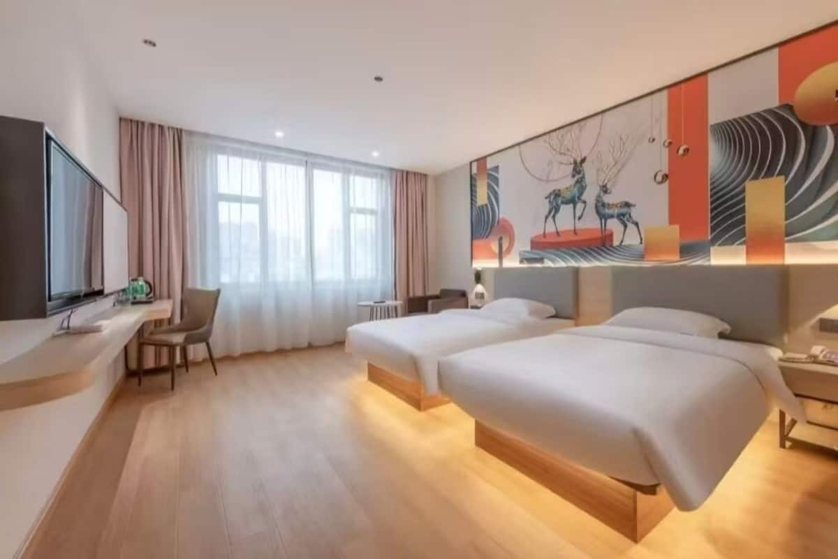 A hotel room with two beds, a desk, a chair, a TV, and a large abstract painting on the wall.