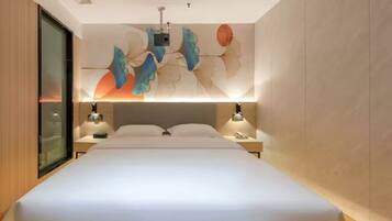 Ein modernes Hotelzimmer mit einem großen Bett, zwei Nachttischen mit Lampen, einem wandmontierten Projektor und einem großflächigen abstrakten Wandbild.
