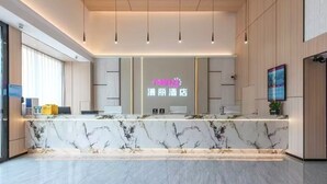 A hotel reception area with a marble counter, a neon sign, and a digital screen displaying information. - Manli Hotel (Foshan)