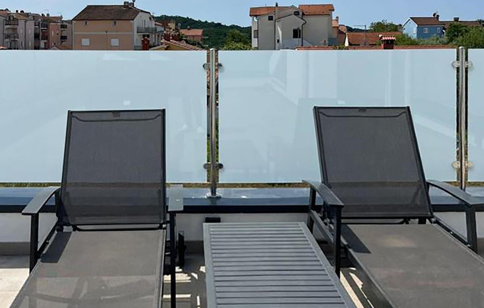 Two sun loungers with metal frames and dark fabric seating, positioned on a rooftop terrace with a view of surrounding buildings.