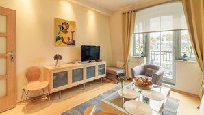 Uma sala de estar moderna com uma televisão de tela plana, um sofá, uma mesa de jantar com uma fruteira e um quadro na parede.
