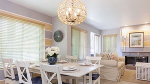 Un comedor con una mesa blanca dispuesta para cuatro personas, rodeado de sillas blancas con cojines azules.