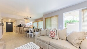 Una sala de estar con un sofá color beige, un área de comedor con una mesa y sillas, y una cocina al fondo.