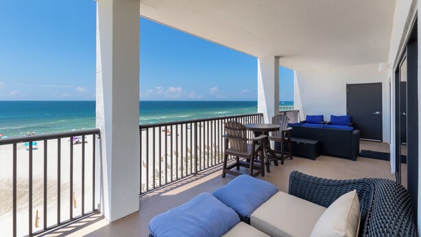 A balcony with a view of the ocean, a seating area with a sofa and chairs, and a small table. - The Palms 501 by Liquid Life (Orange Beach)