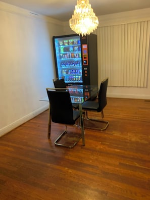 Una habitación con una mesa de comedor, dos sillas, una máquina expendedora y una araña.