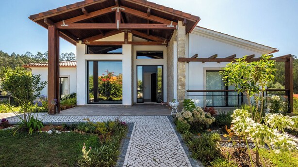 A modern house with a covered porch, large windows, and a garden with various plants and flowers. - Contemporary rural villa with large wooden beams with artistic accents (parracheira, Arrabal)