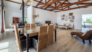 A spacious living room with a high ceiling, exposed wooden beams, a glass dining table, wicker chairs, a brown leather sofa, and a television. - Contemporary rural villa with large wooden beams with artistic accents (parracheira, Arrabal)