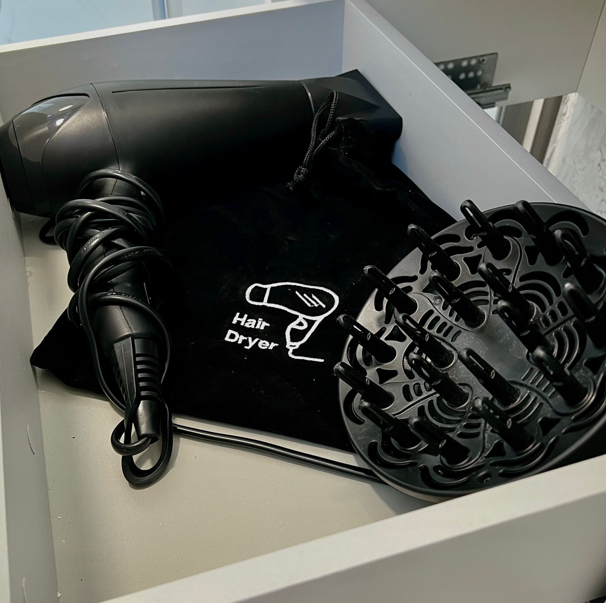 A black hair dryer with a cord, placed in a white drawer.