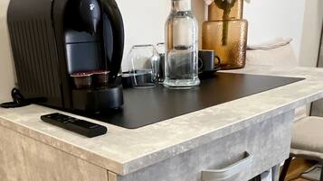 A compact kitchenette with a coffee maker, a bottle, and a vase with flowers.