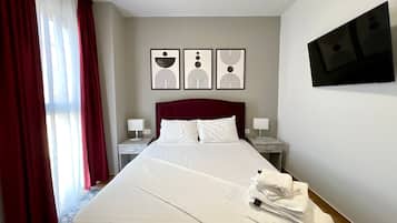 Una habitación de hotel con una cama grande, dos mesitas de noche con lámparas, una cortina roja y tres cuadros en la pared.