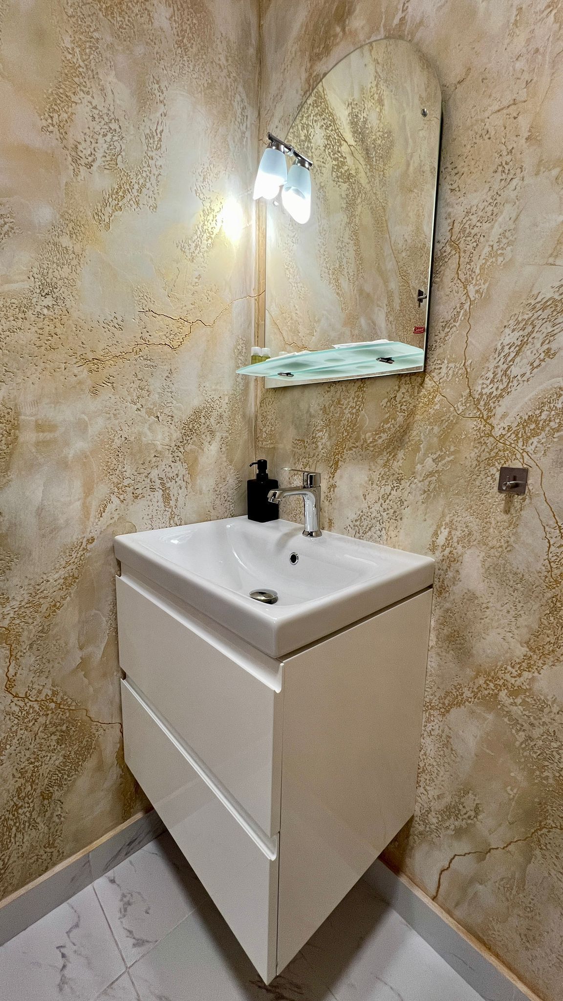 A bathroom with a white sink, a mirror, and a wall-mounted light fixture.