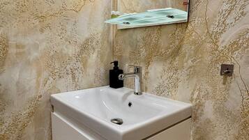 A bathroom with a white sink, a mirror, and a wall-mounted light fixture.