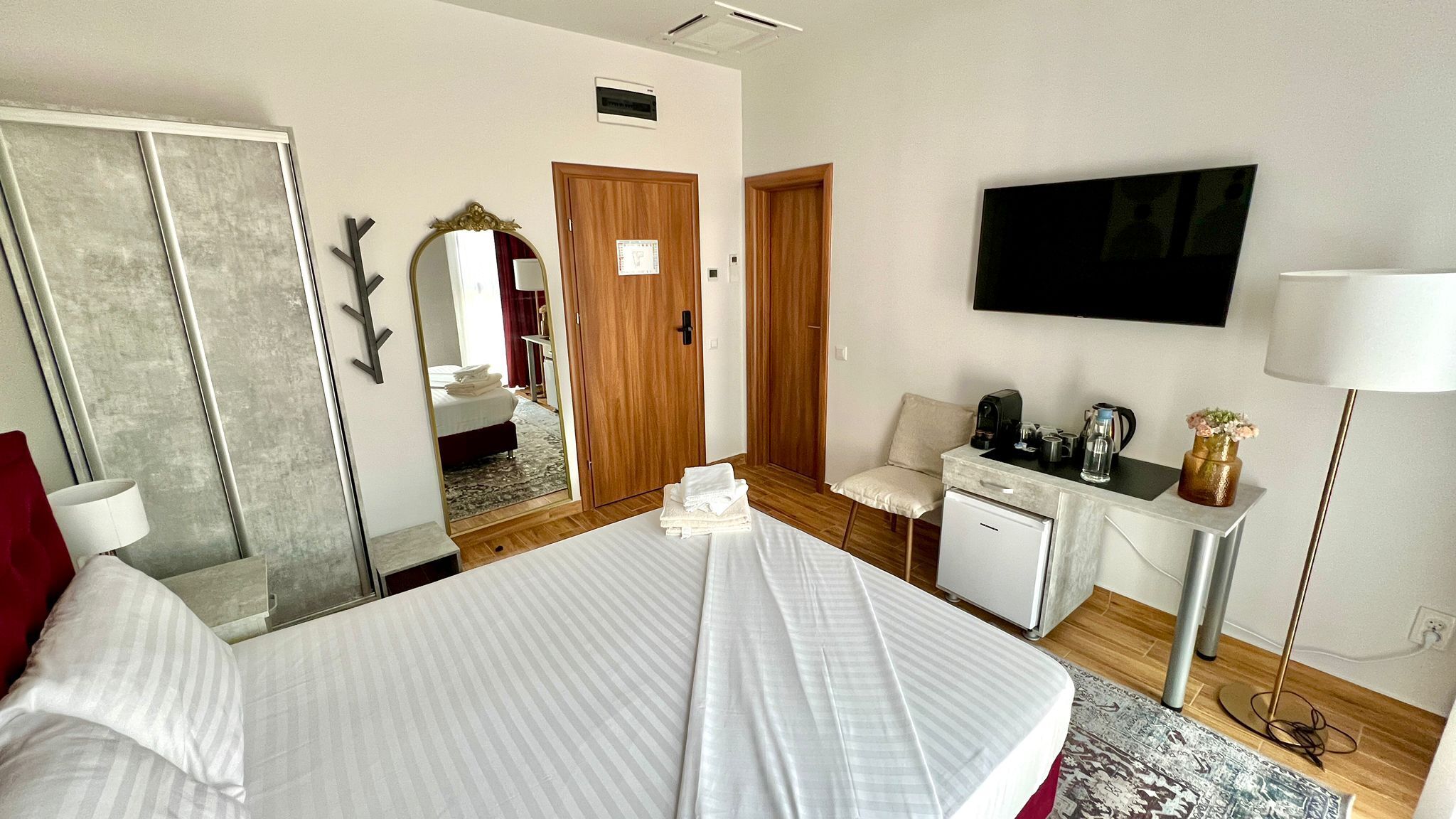 Habitació d'hotel amb un llit, una taula de treball amb una cadira, un televisor i un mirall.