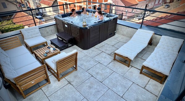 Una terraza en la azotea con jacuzzi, muebles de madera y sillones de descanso.