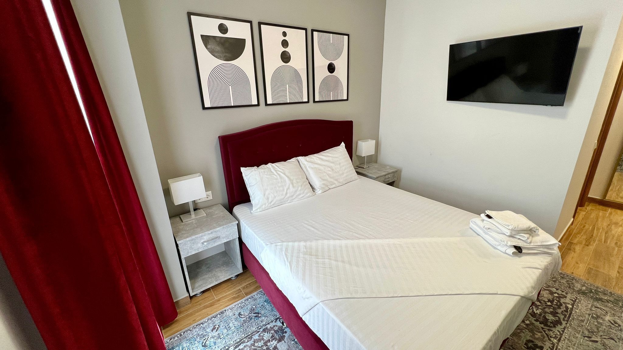 Una cama bien hecha con sábanas blancas, un cabecero rojo y un televisor de pantalla plana montado en la pared.