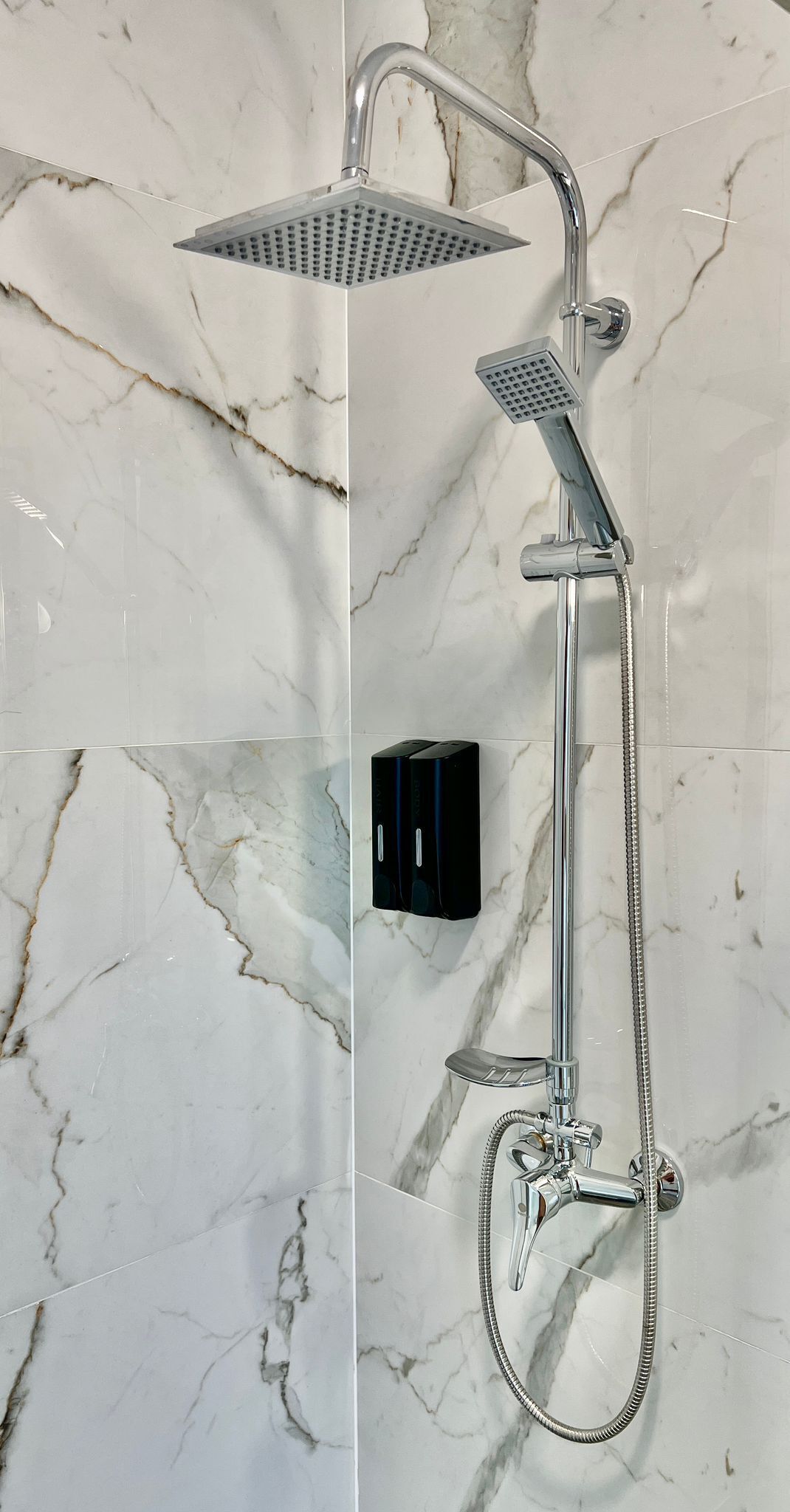 A modern shower with a handheld showerhead, a fixed showerhead, and a handheld shower hose.