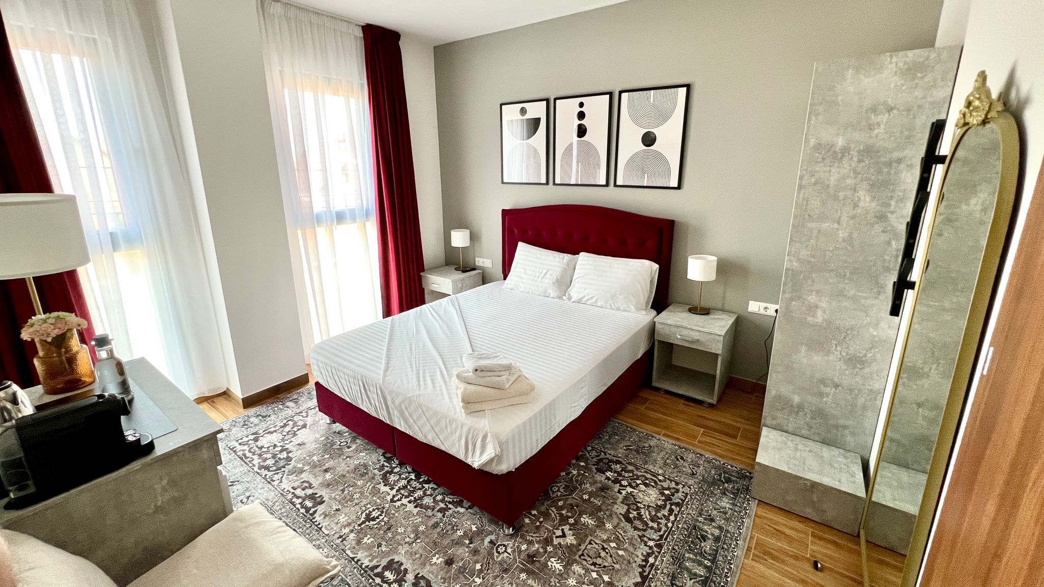 A neatly arranged hotel room with a large bed, bedside tables, a mirror, and artwork on the wall.