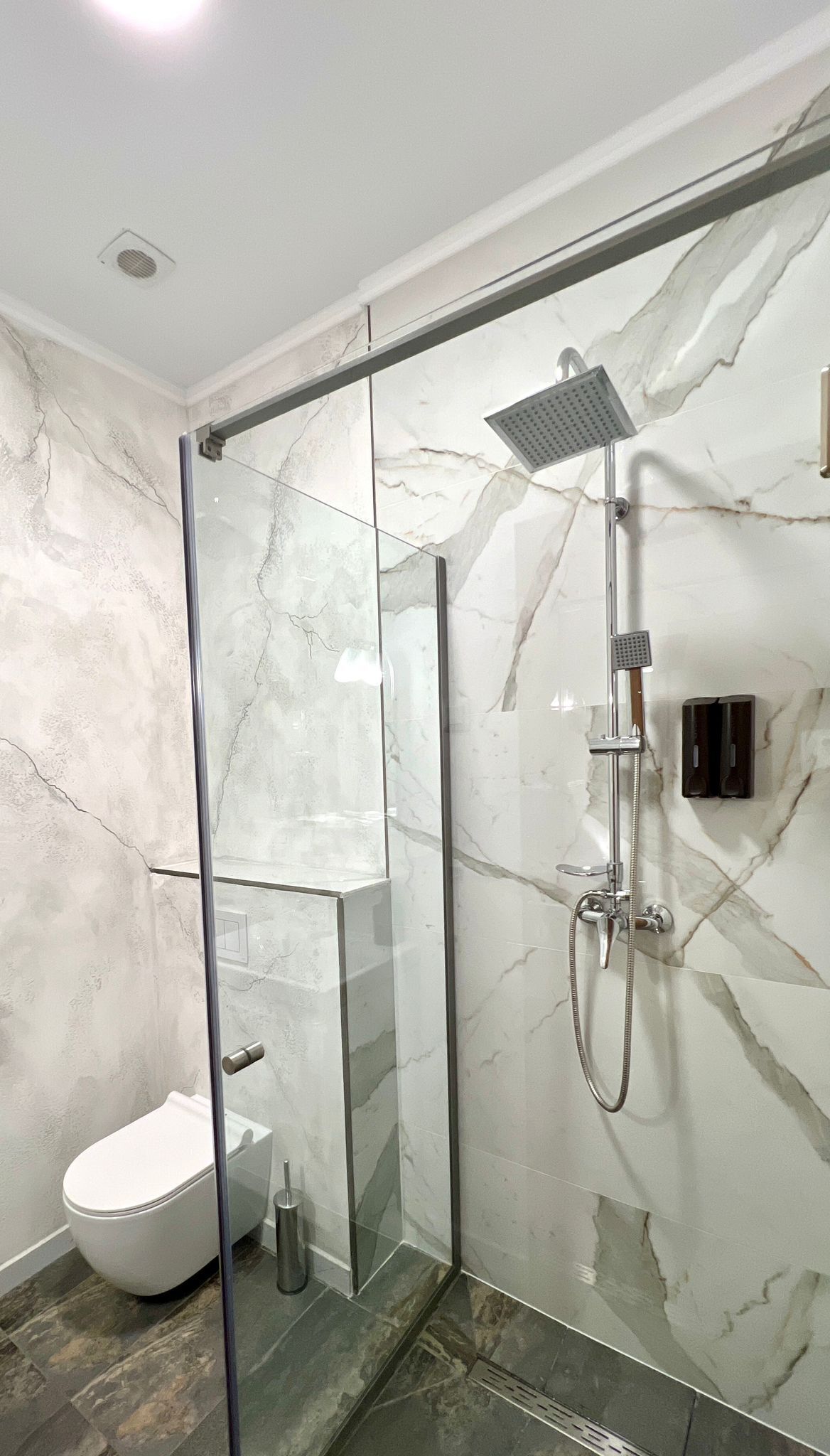A modern bathroom with a glass-enclosed shower, a white toilet, and marble walls.