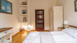 A bedroom with a wooden floor, a bed with white linens, a wooden nightstand, a white wardrobe, and a shelf with framed pictures. - Red by Grand Apartments (Sopot)